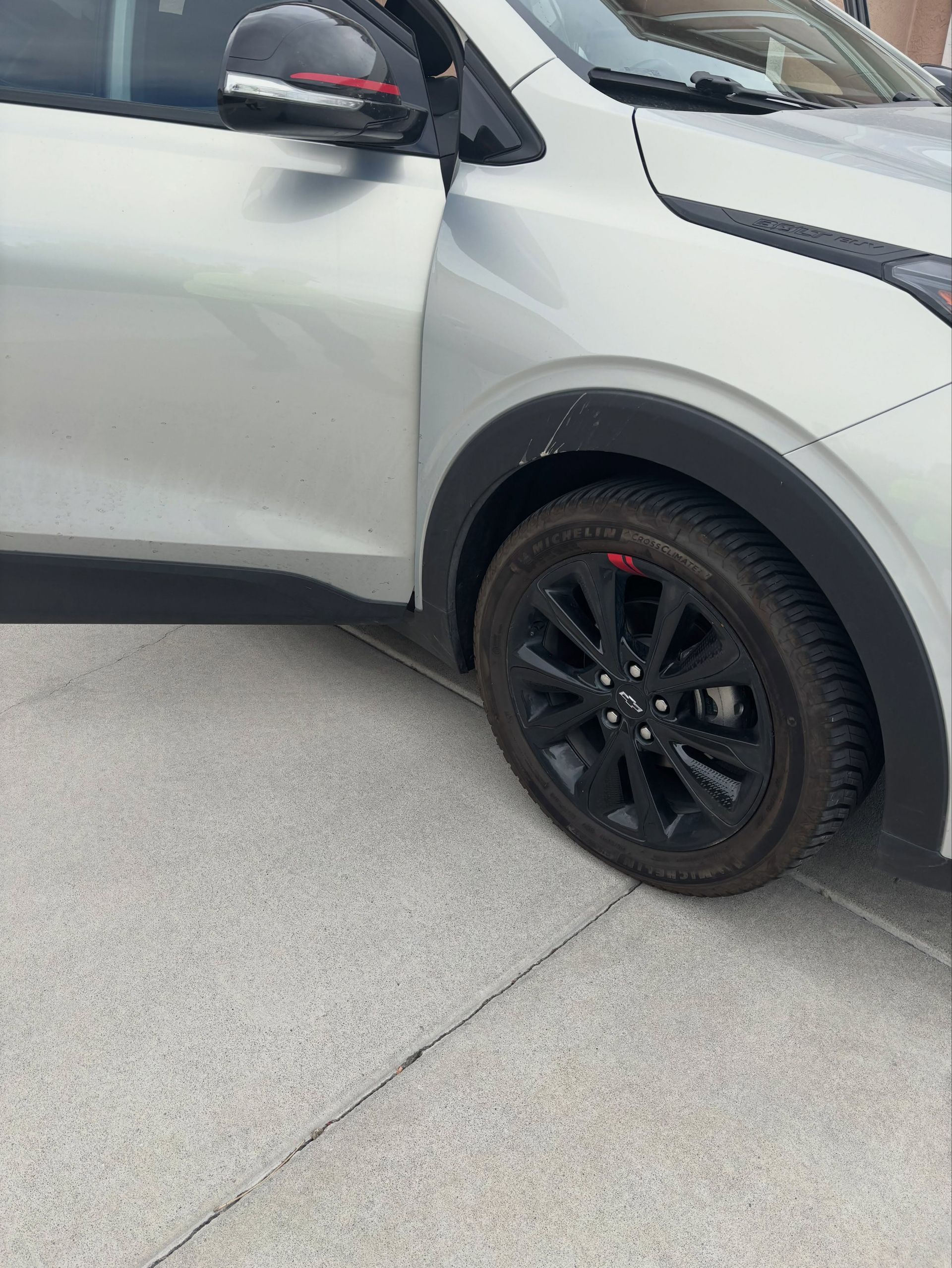Silver SUV with black wheel parked on a concrete driveway, driver door open