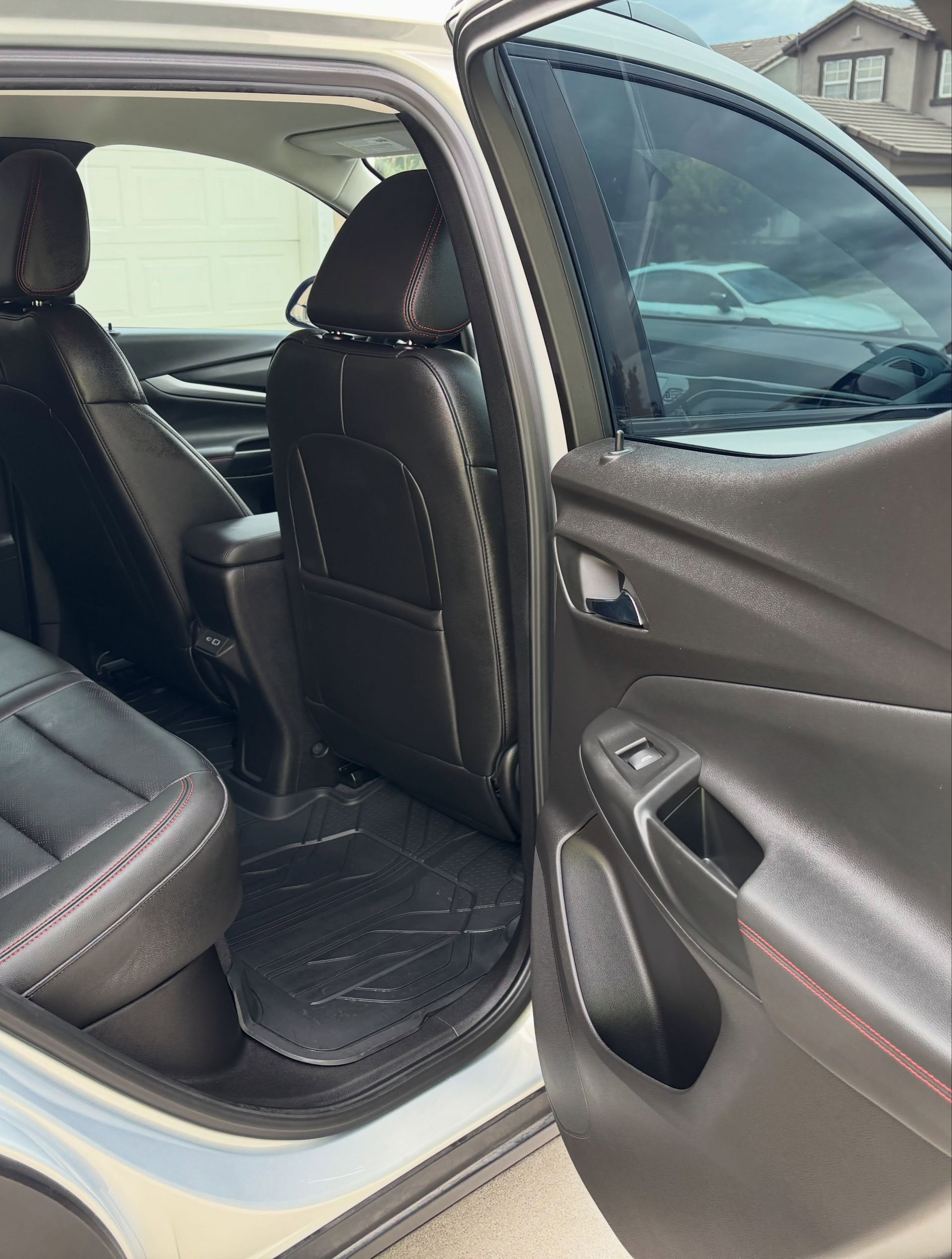 Rear car seat with black leather seats and an open door, showing the interior and window controls