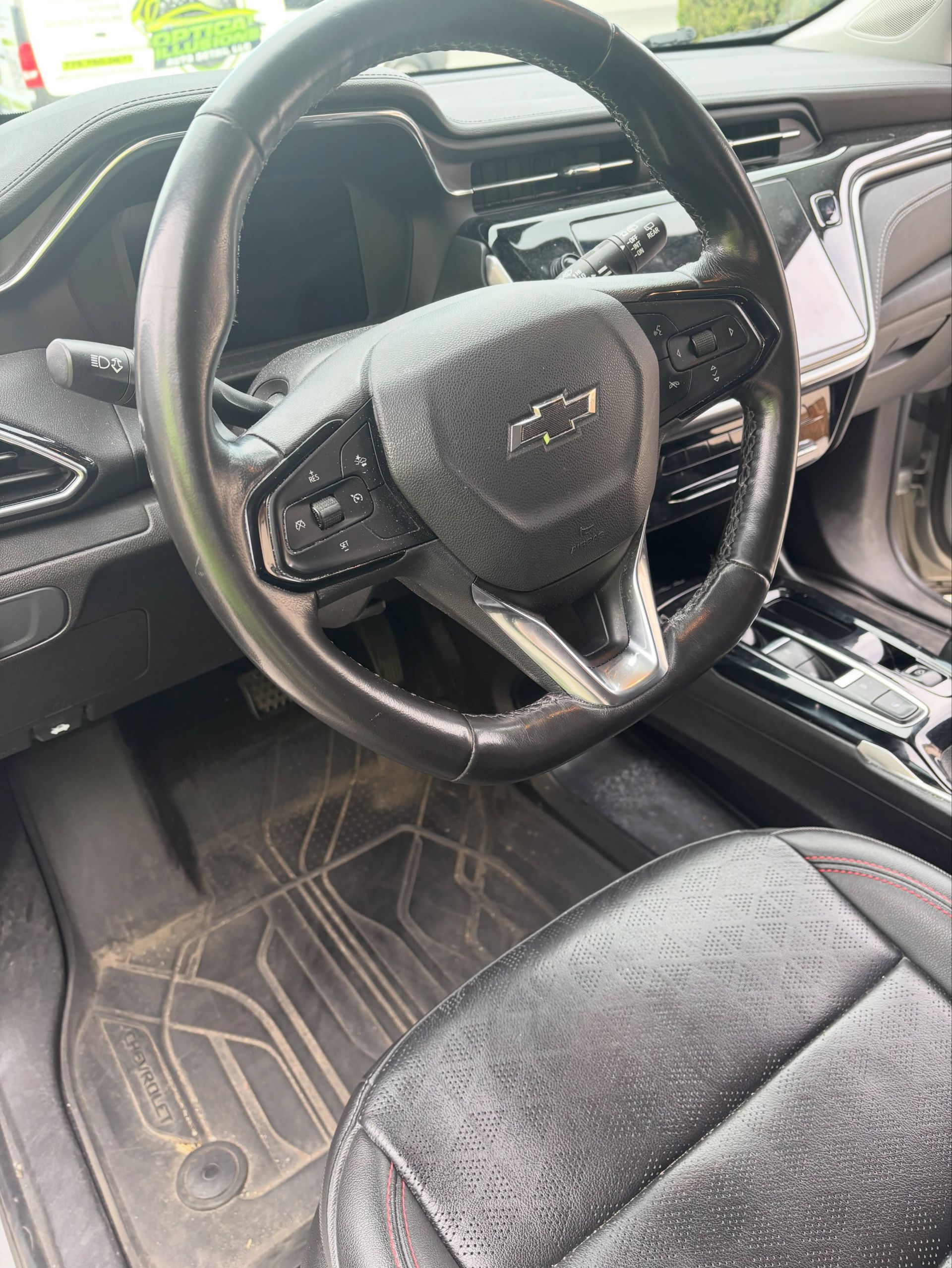 Chevrolet car interior with black steering wheel, dashboard, center console, and floor mat visible