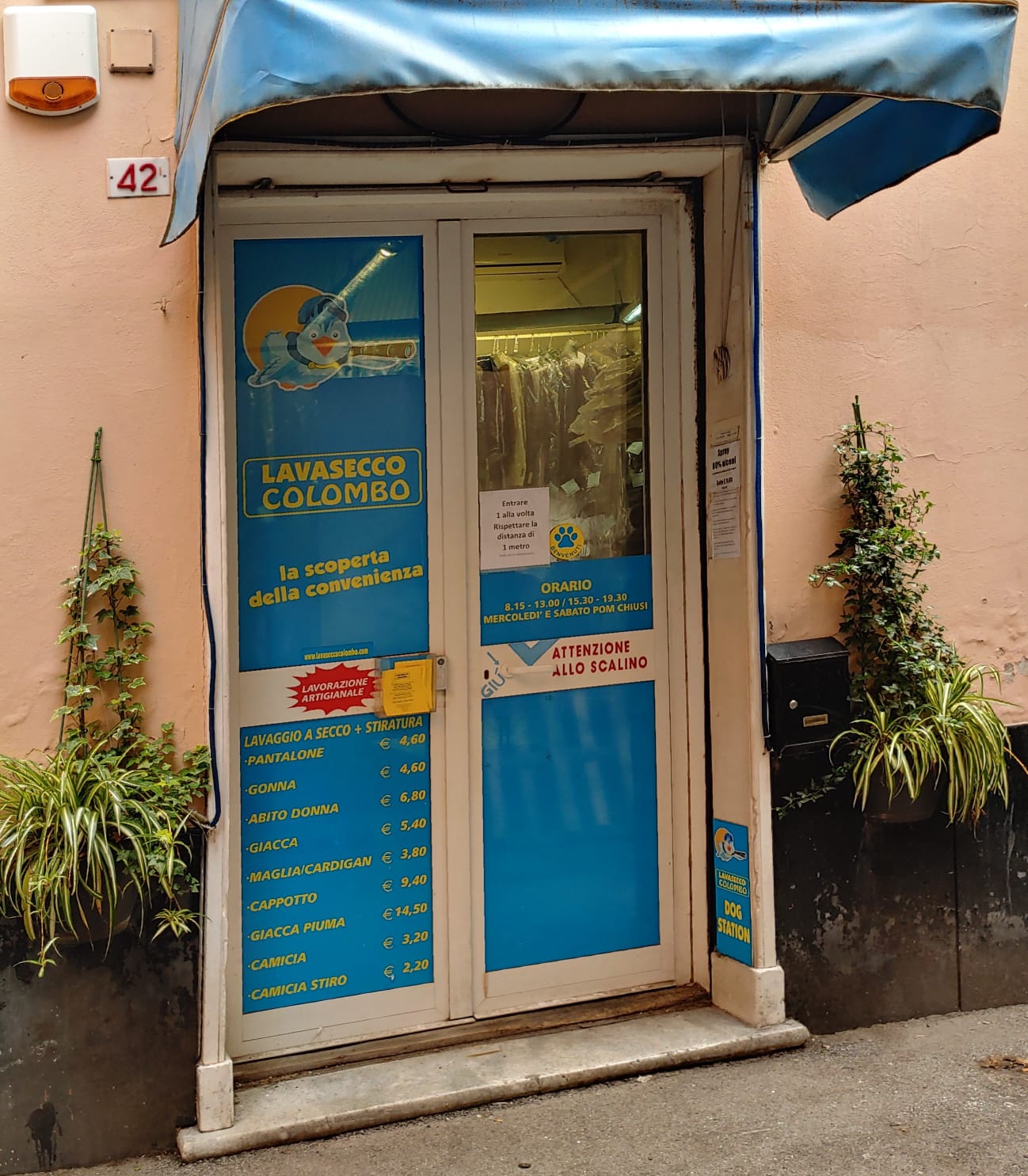 L'ingresso di una lavanderia a secco in Italia con una tenda blu e un listino prezzi sulla porta.