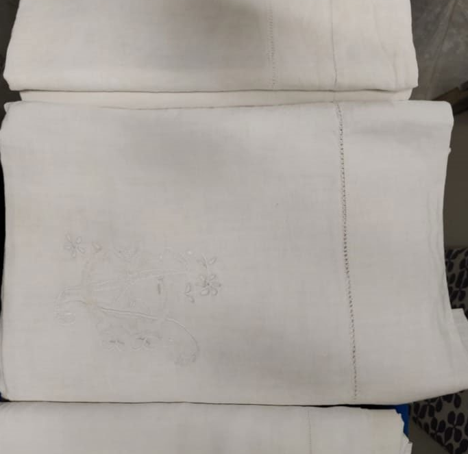 Lenzuola bianche piegate e impilate, disegno ricamato sulla parte superiore, bordo cucito.