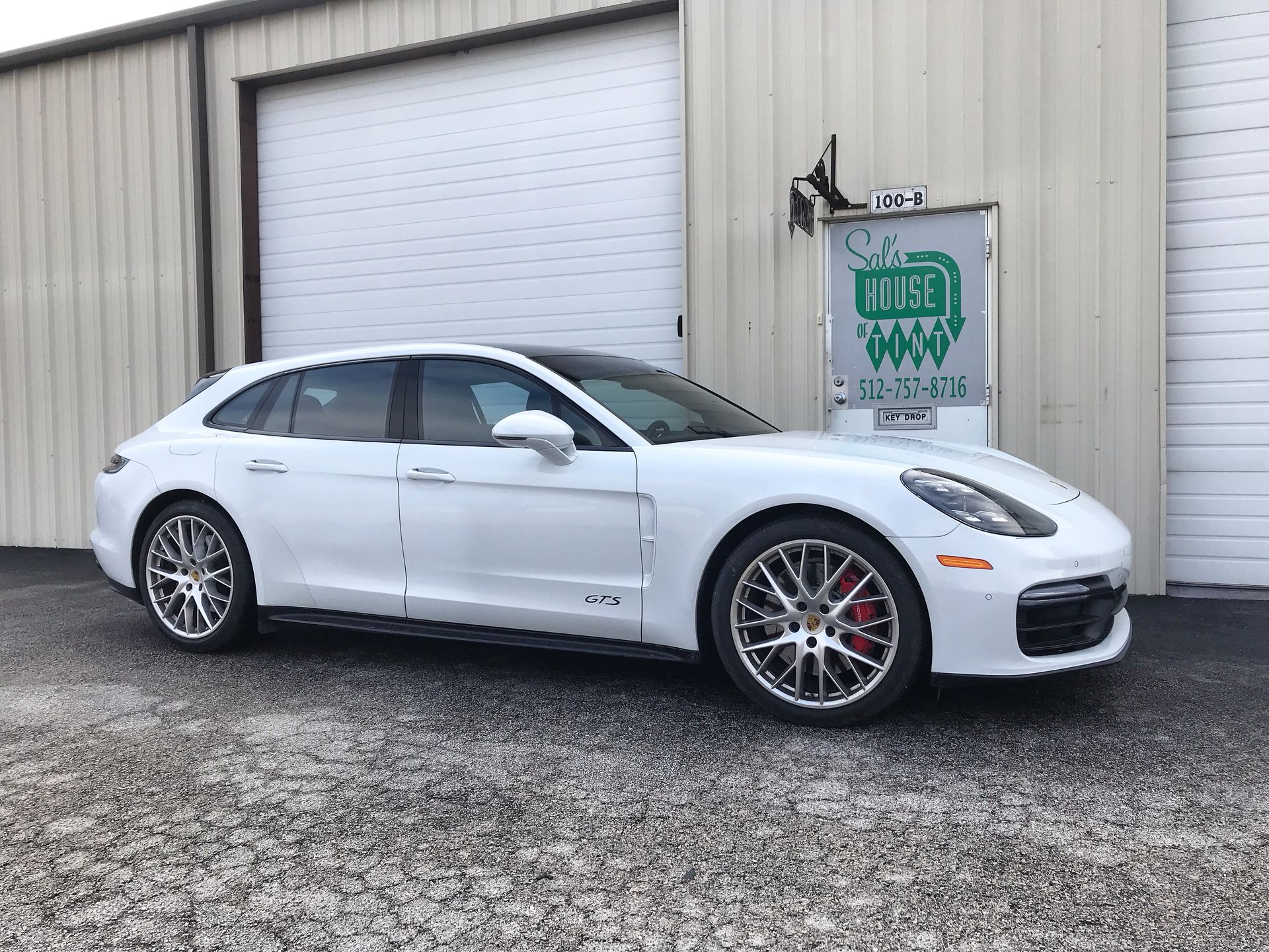 White sedan parked outside a garage beside a metal building.