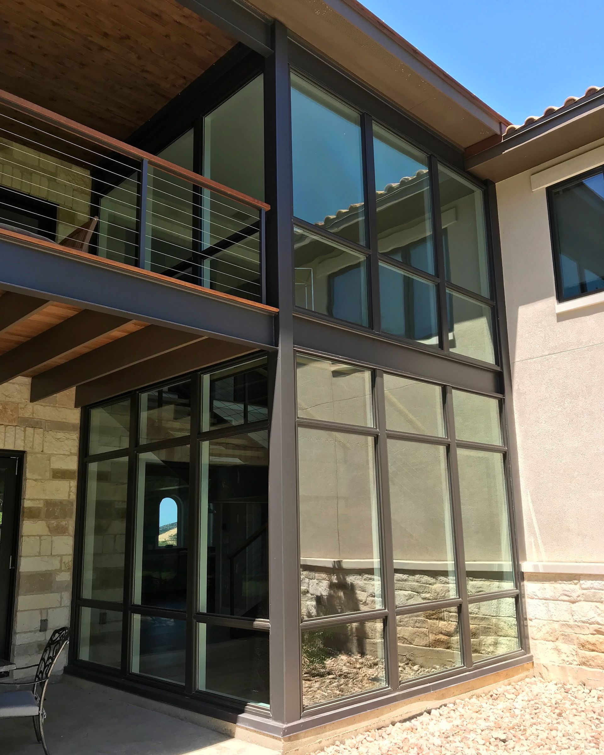 Modern house exterior with a glass corner sunroom, balcony, and stone-accented walls