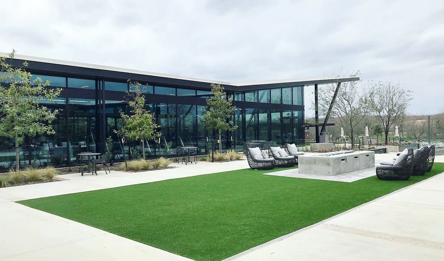 Modern glass office building with a green lawn and outdoor lounge seating in front