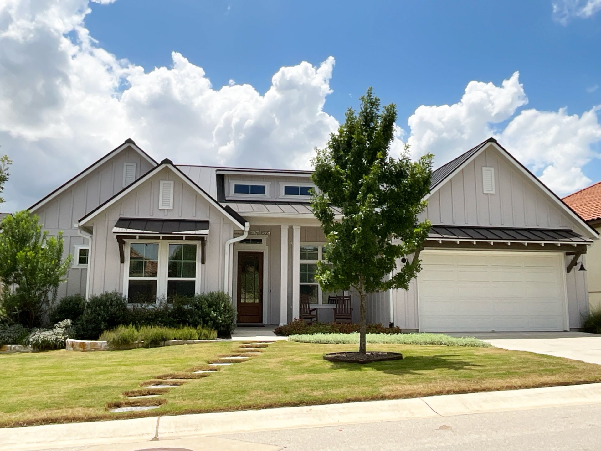 Single-story suburban house with white exterior, front lawn, and two-car garage under a partly cloudy sky