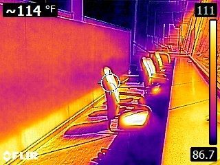 Thermal image of a person holding a hose beside a wall, with hot surfaces and temperature readings visible.