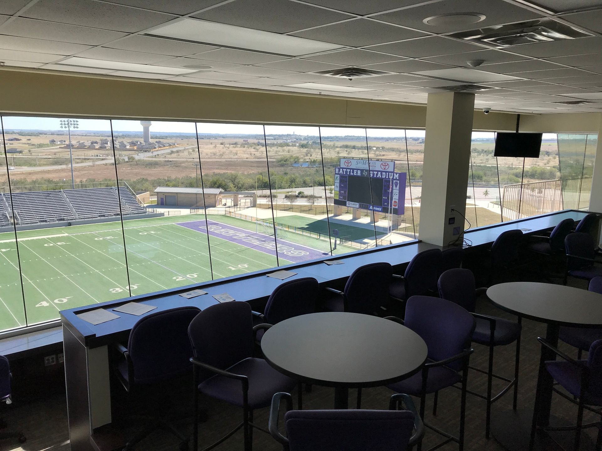 Covered stadium seating overlooking a football field and scoreboard on a sunny day