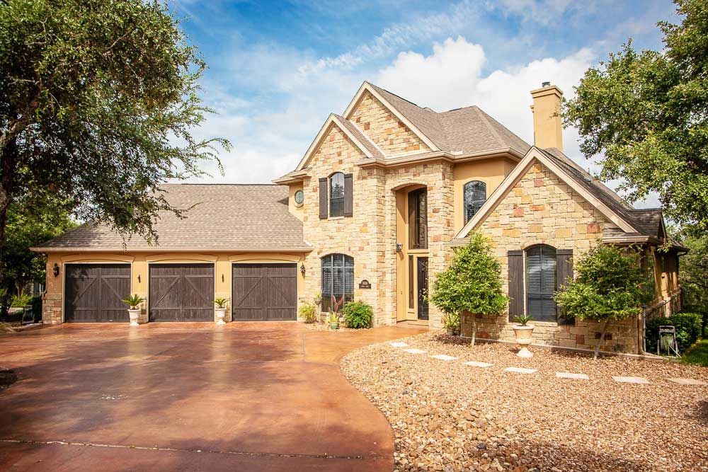 Stone house with three-car garage, brown driveway, and landscaped front yard under a blue sky