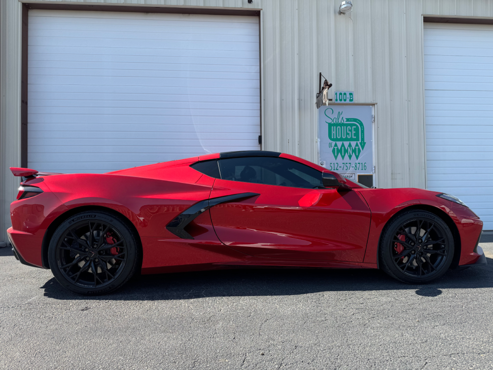 Red sports car parked beside a garage door and utility box.