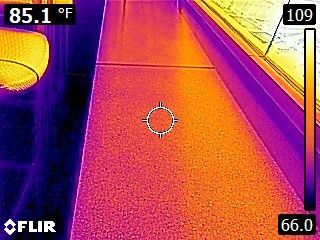 Thermal view of a sunlit pavement with a crosshair centered on the ground and temperature scale at right