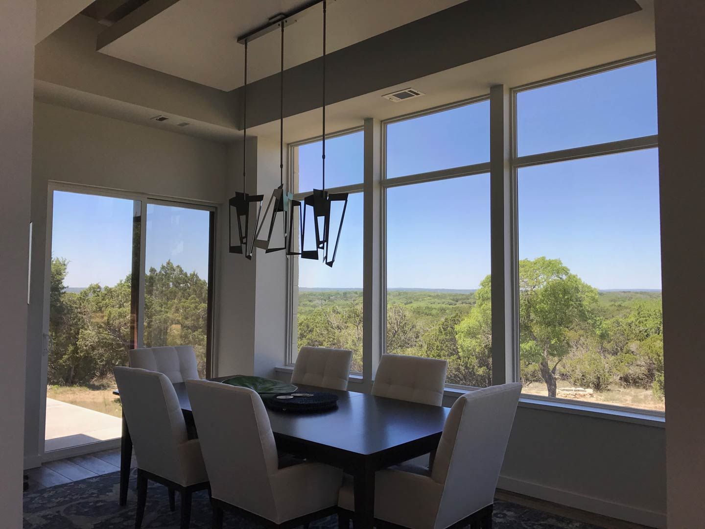 Dining room with table and chairs beside large windows overlooking trees and blue sky