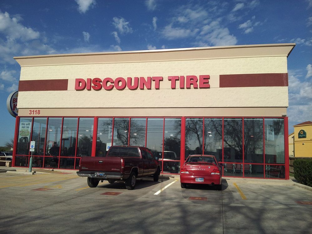 Discount Tire storefront with red windows and two parked vehicles out front