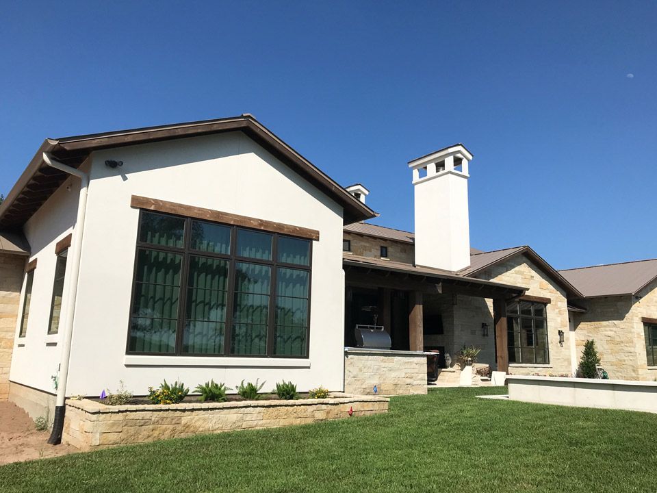 Modern single-story house with white stucco, stone accents, and a green lawn under a clear blue sky