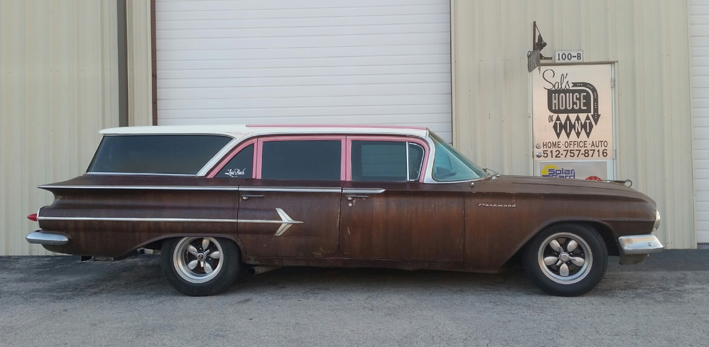 Brown vintage station wagon parked beside a beige building, side view