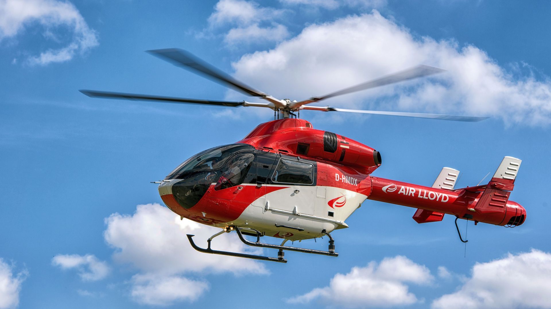Red and white helicopter flying against a blue sky with clouds