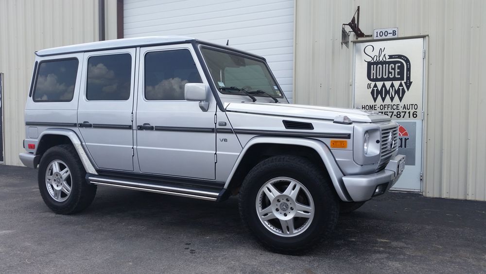 Silver Mercedes G-Class SUV parked outside a building with a sign on the wall