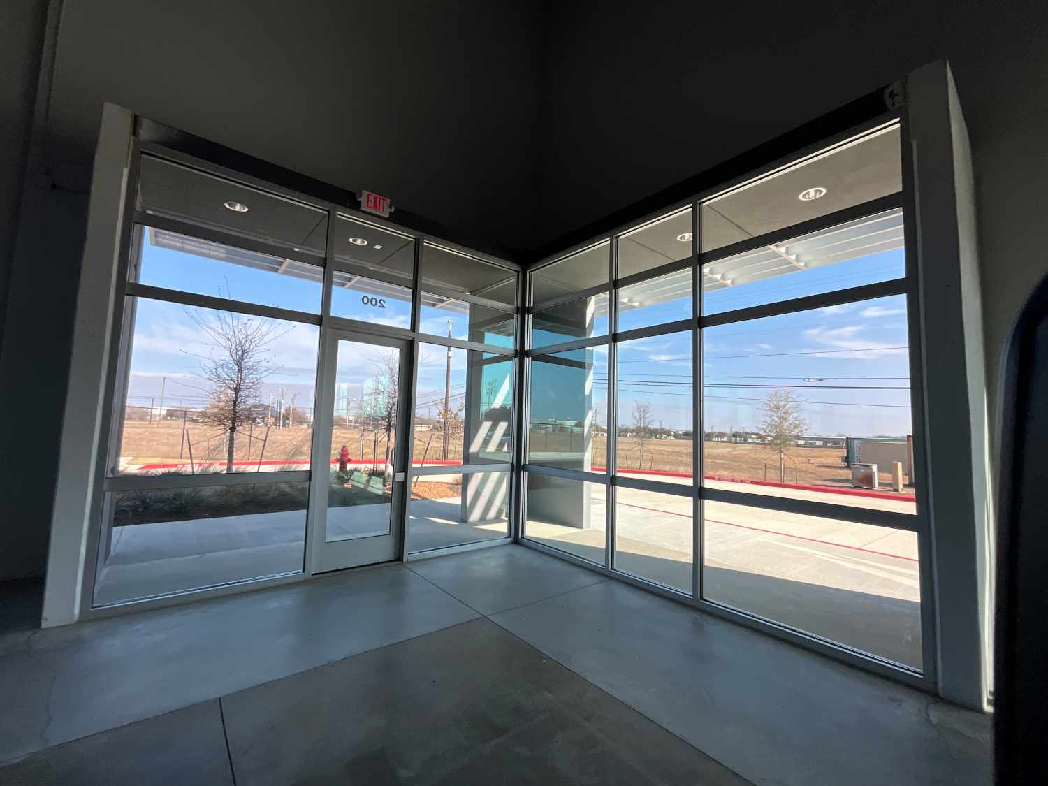 Empty storefront interior with floor-to-ceiling glass windows and doors opening to a street outside