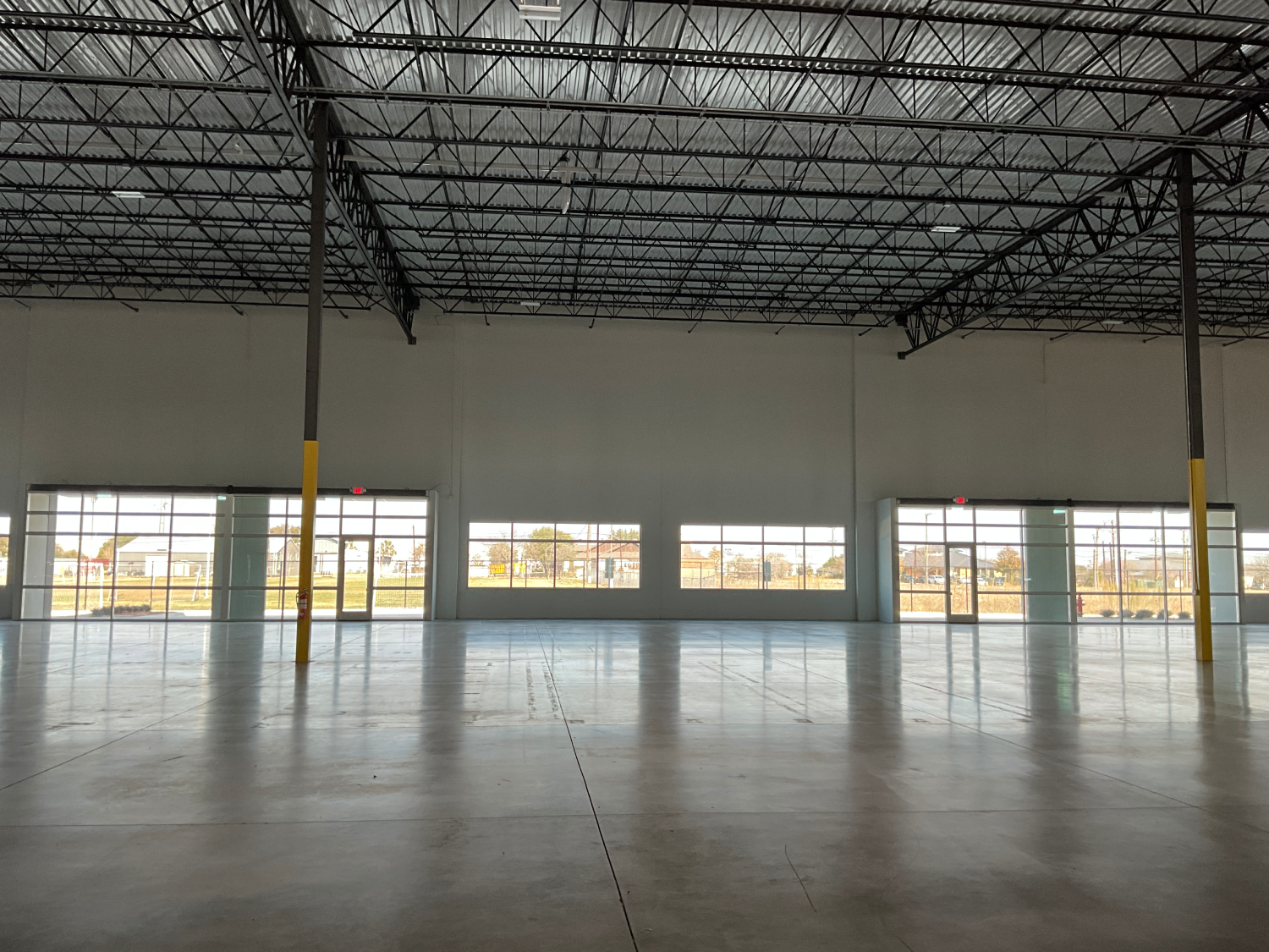 Empty warehouse interior with polished concrete floor, exposed ceiling, and large windows along one wall