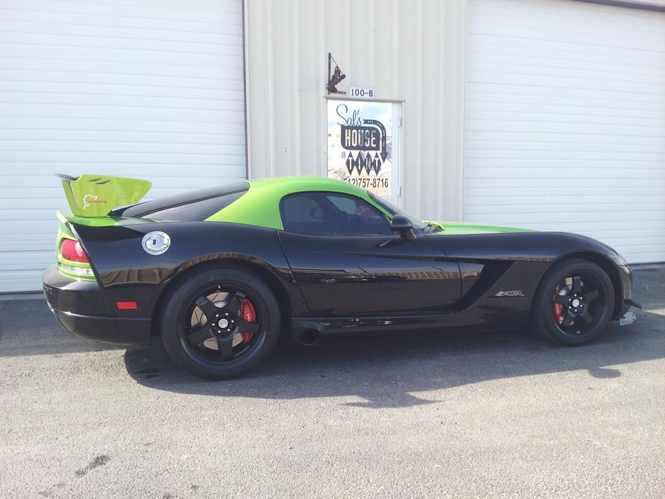 Black sports car with a bright green hood in front of a white garage door