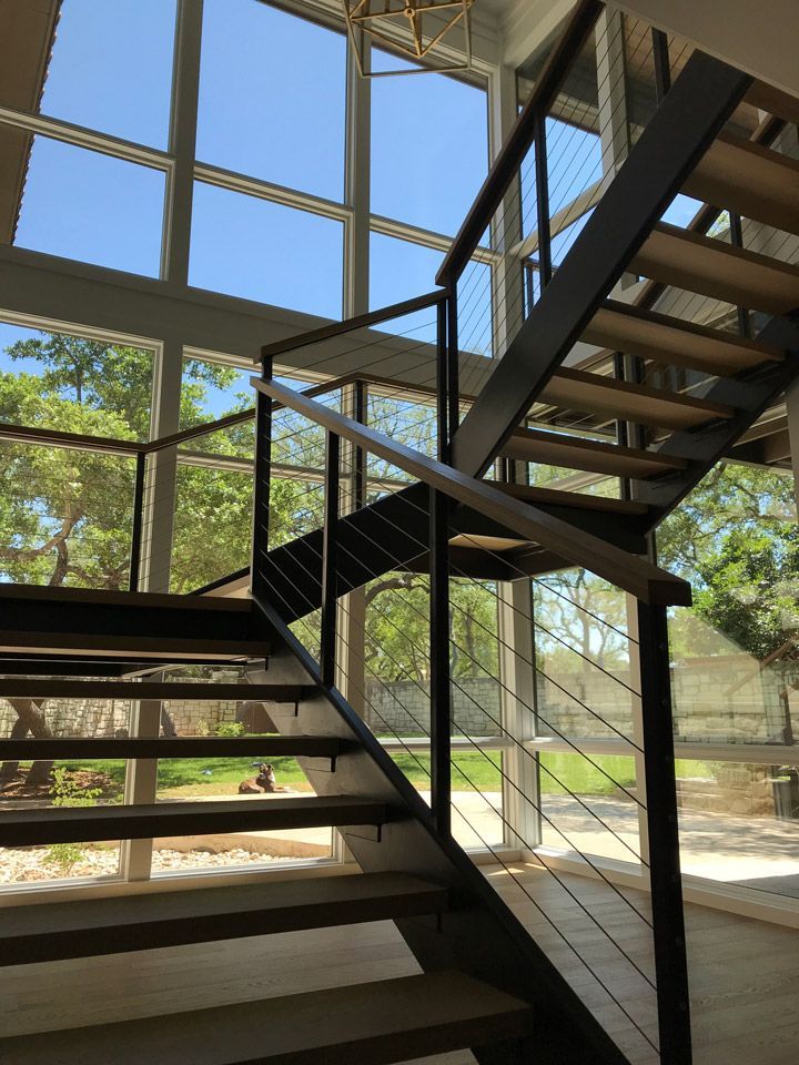 Modern black metal staircase inside a glass-walled building with sunlight and trees outside