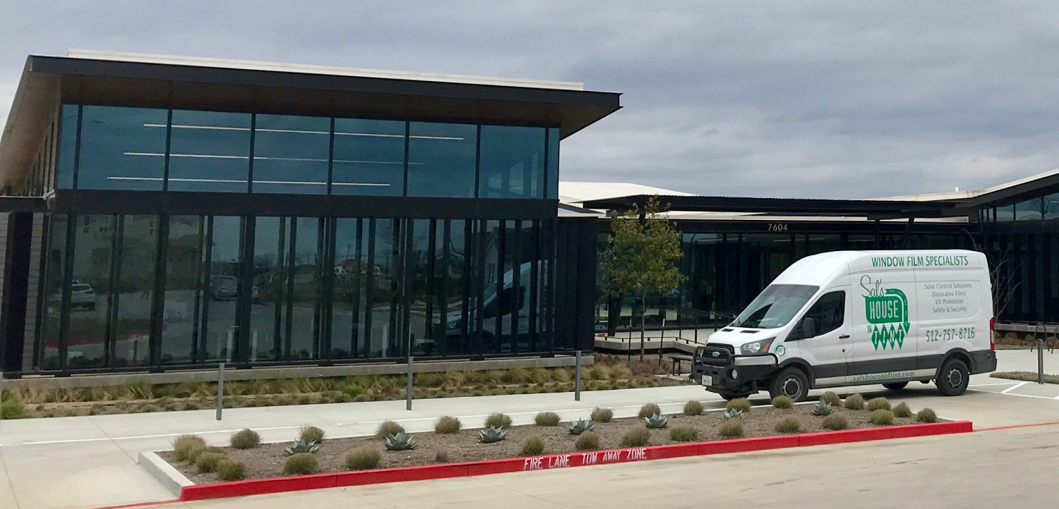 Modern glass office building beside a white service van in a parking lot