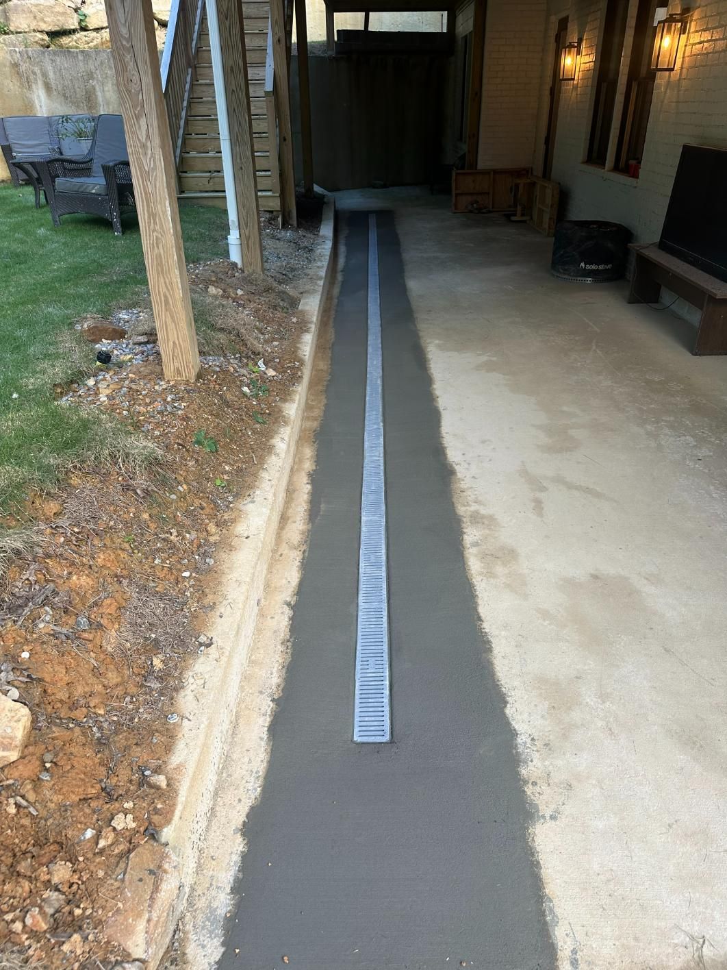Concrete driveway with a long, central drain. A building is visible in the background.