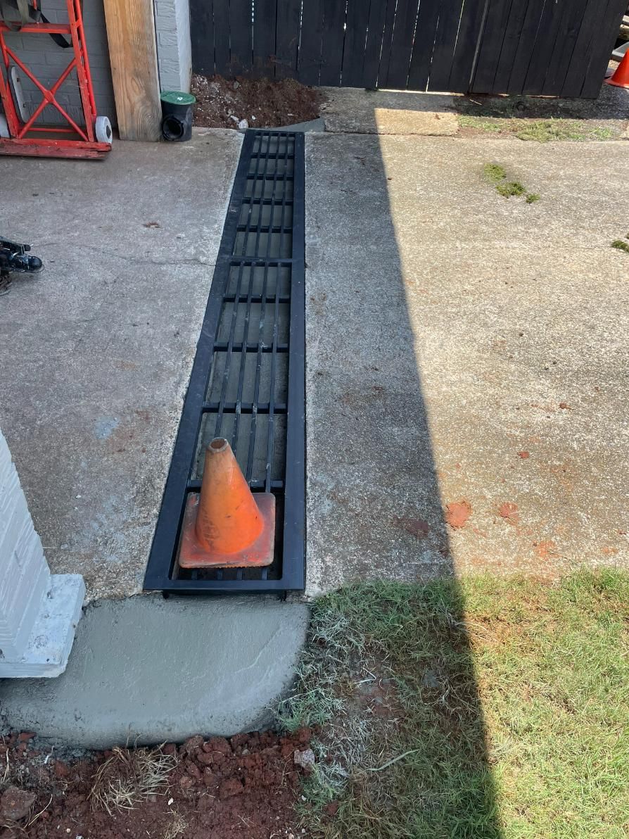 Concrete drainage grate with an orange traffic cone, next to a concrete driveway and grass.
