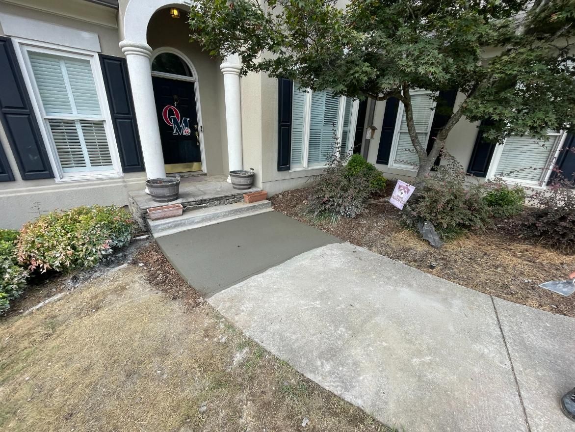 Front entrance with newly poured concrete pathway, house with black shutters, and small tree.