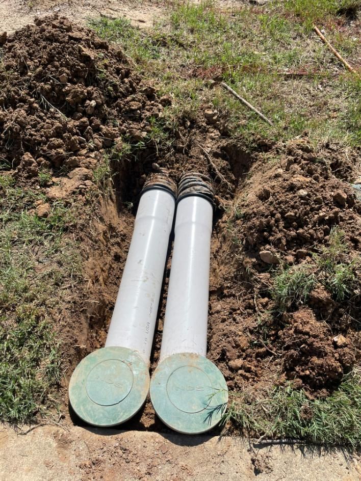 Two white pipes with green lids emerge from dirt, set in a grassy area.