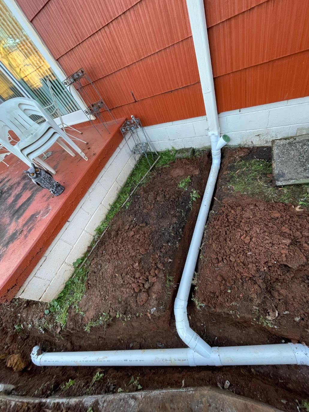 White gutter pipe and downspout diverting rainwater underground from a red house.