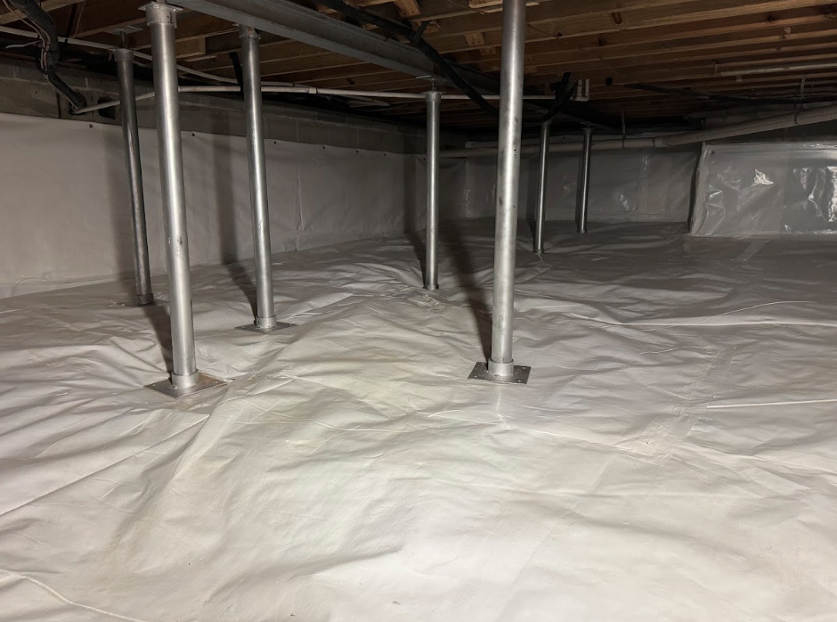 Basement with white wrapped walls and metal supports, leading to an open door and a yard.