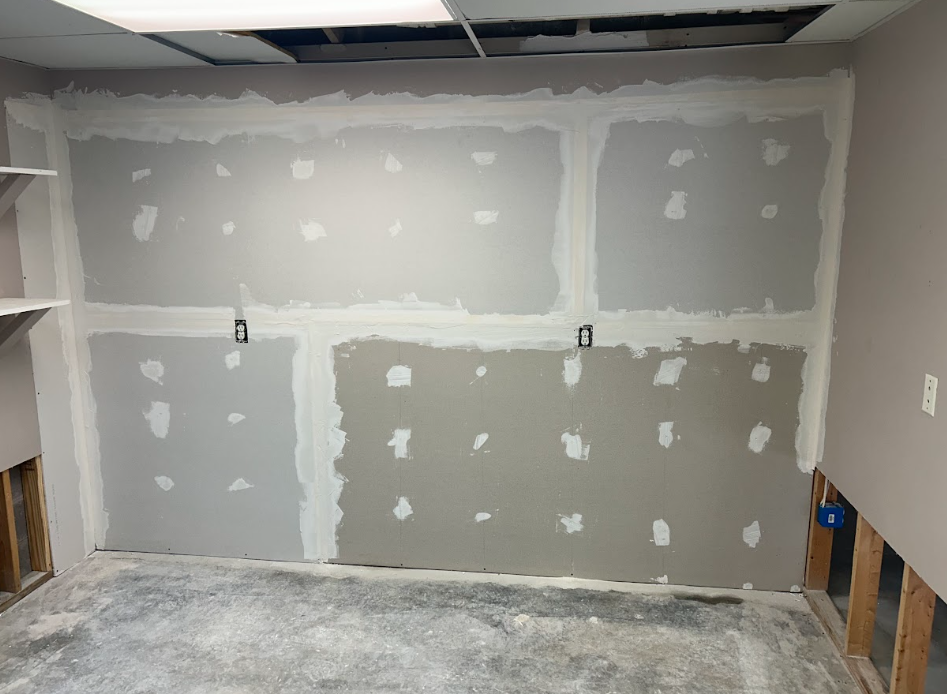 Basement with white wrapped walls and metal supports, leading to an open door and a yard.
