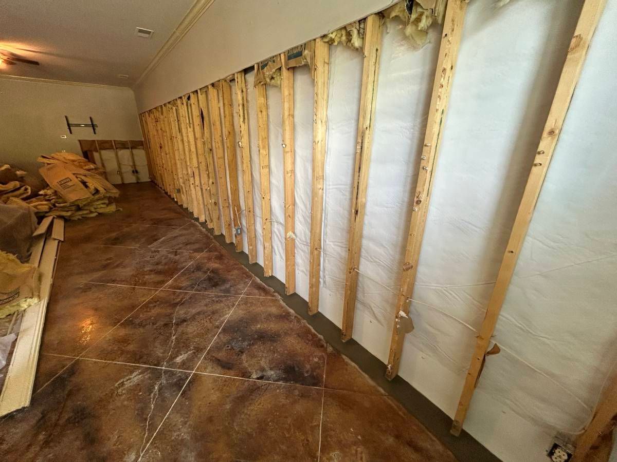 Basement with white wrapped walls and metal supports, leading to an open door and a yard.