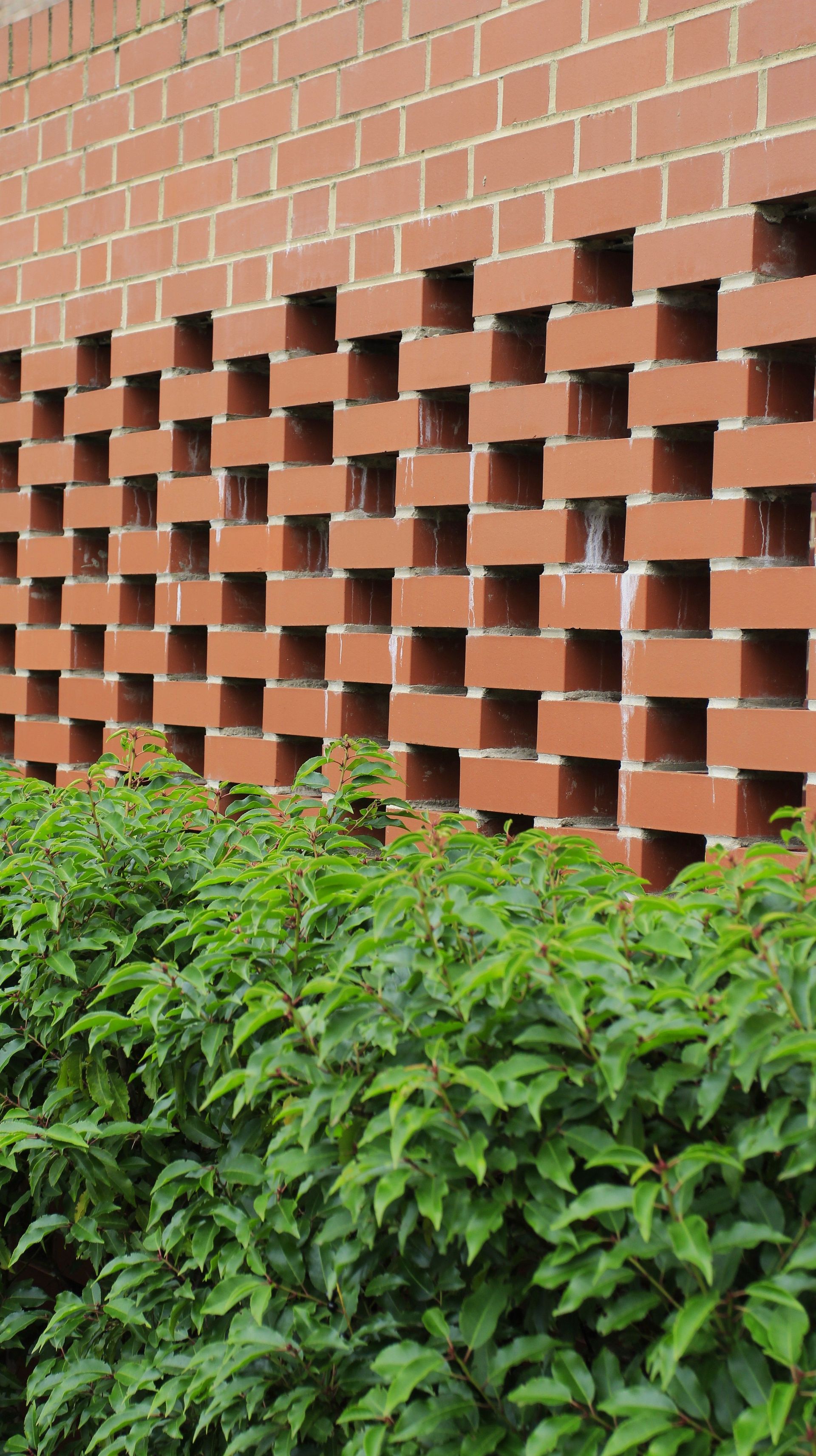 Red brick wall with staggered brick openings above green shrubs