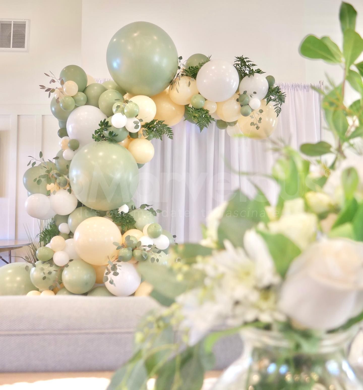 A vase of flowers is sitting in front of a couch covered in balloons.
