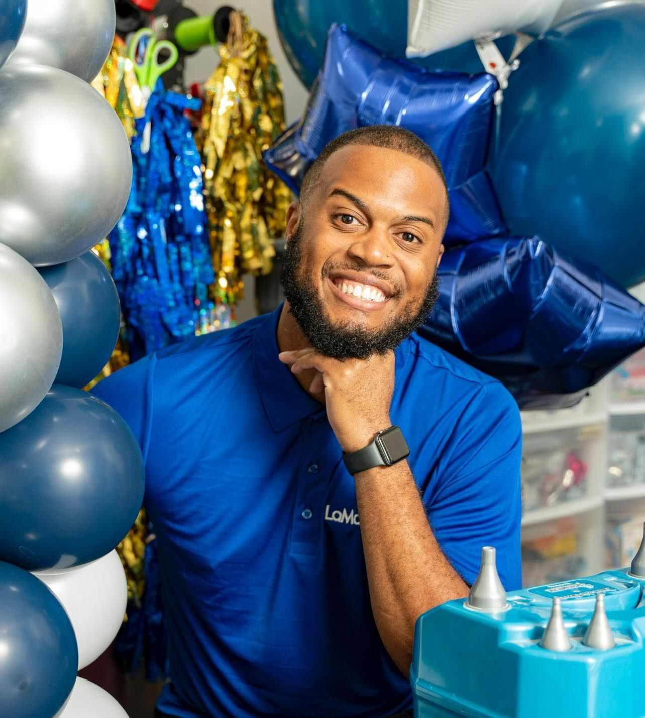 A man in a blue shirt is standing in front of a bunch of balloons.