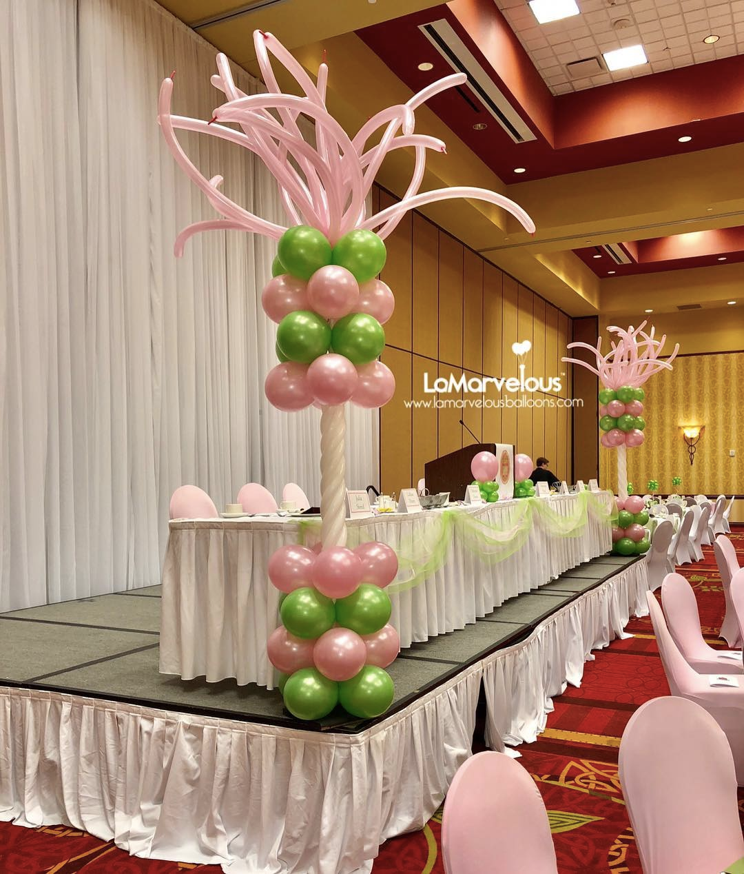 A room with a table and chairs decorated with pink and green balloons