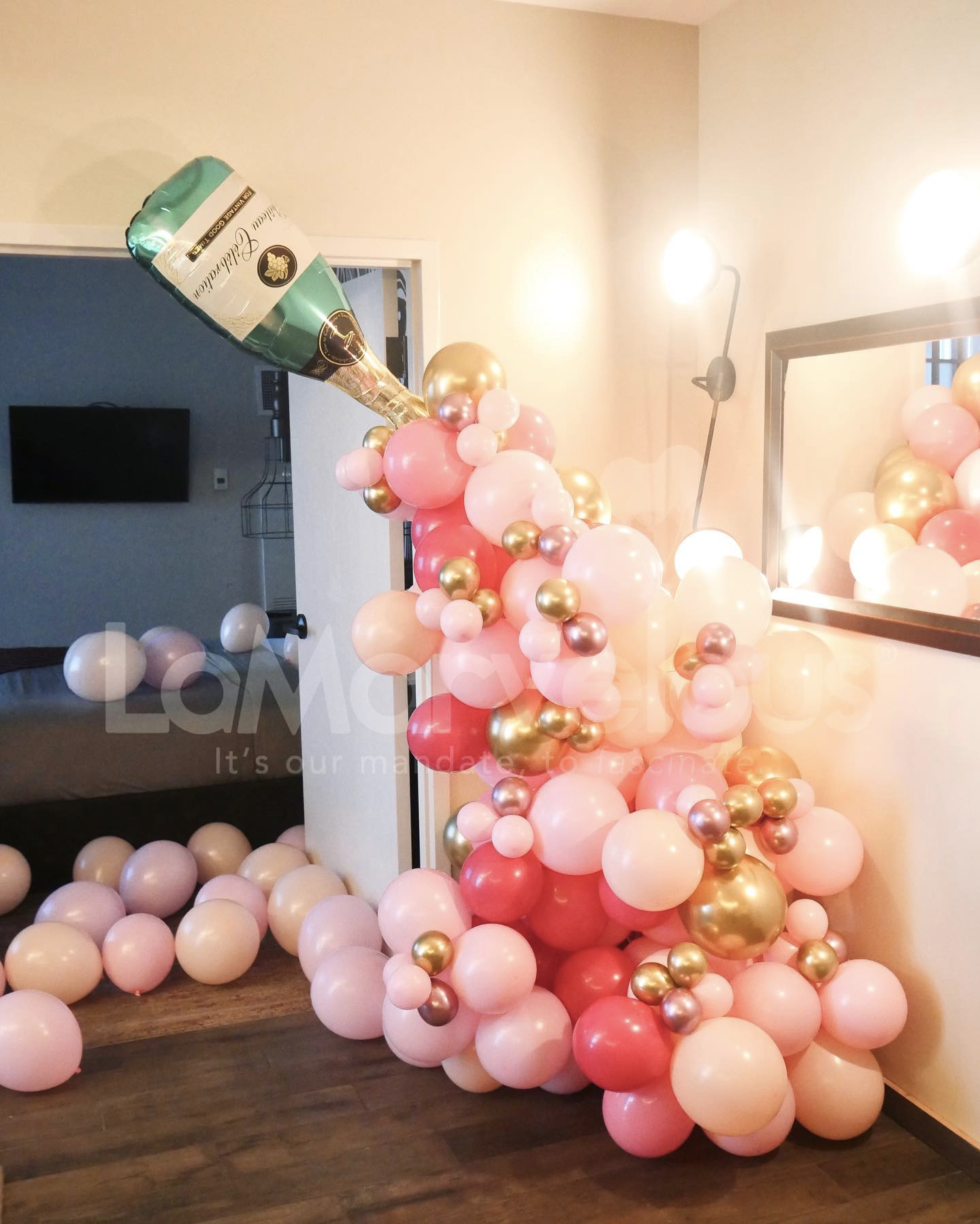 A room filled with pink and gold balloons and a bottle of champagne