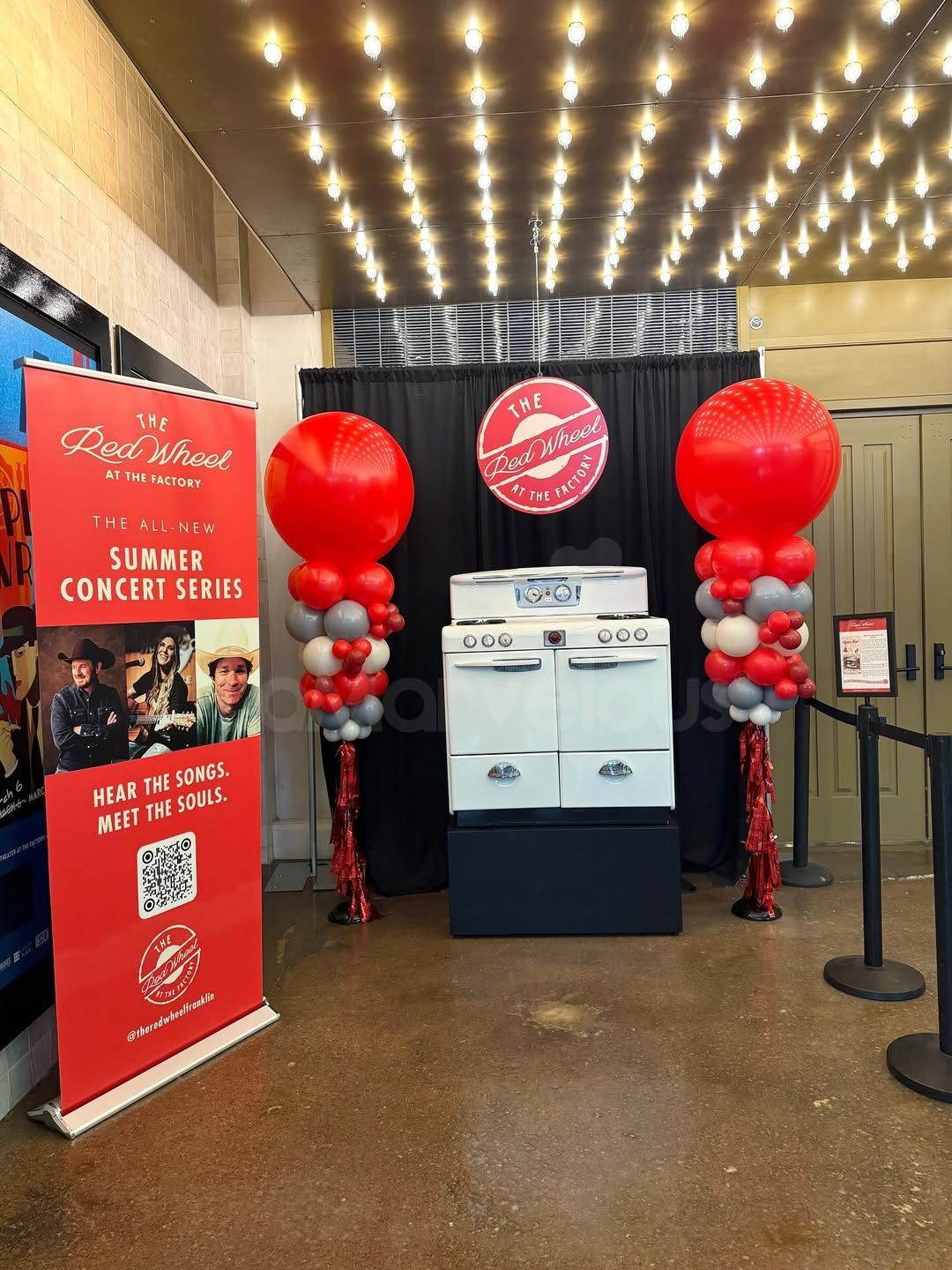 Red and white balloon decorations flank a display of a new appliance at a trade show.