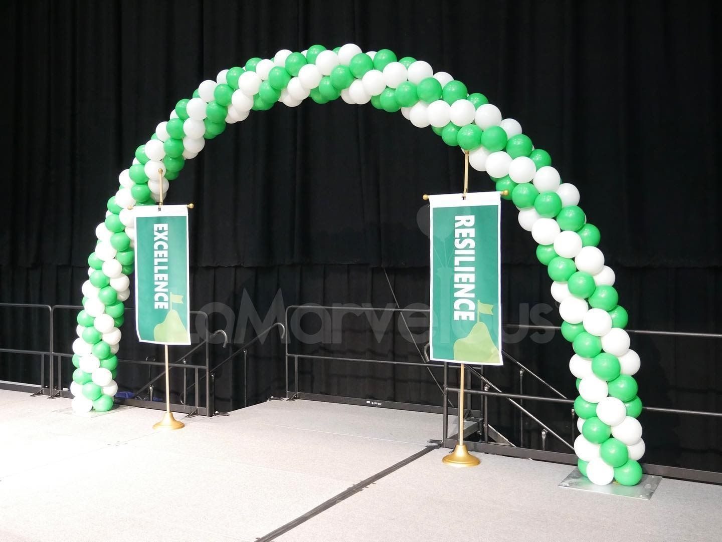 A green and white balloon arch with banners that say resilience