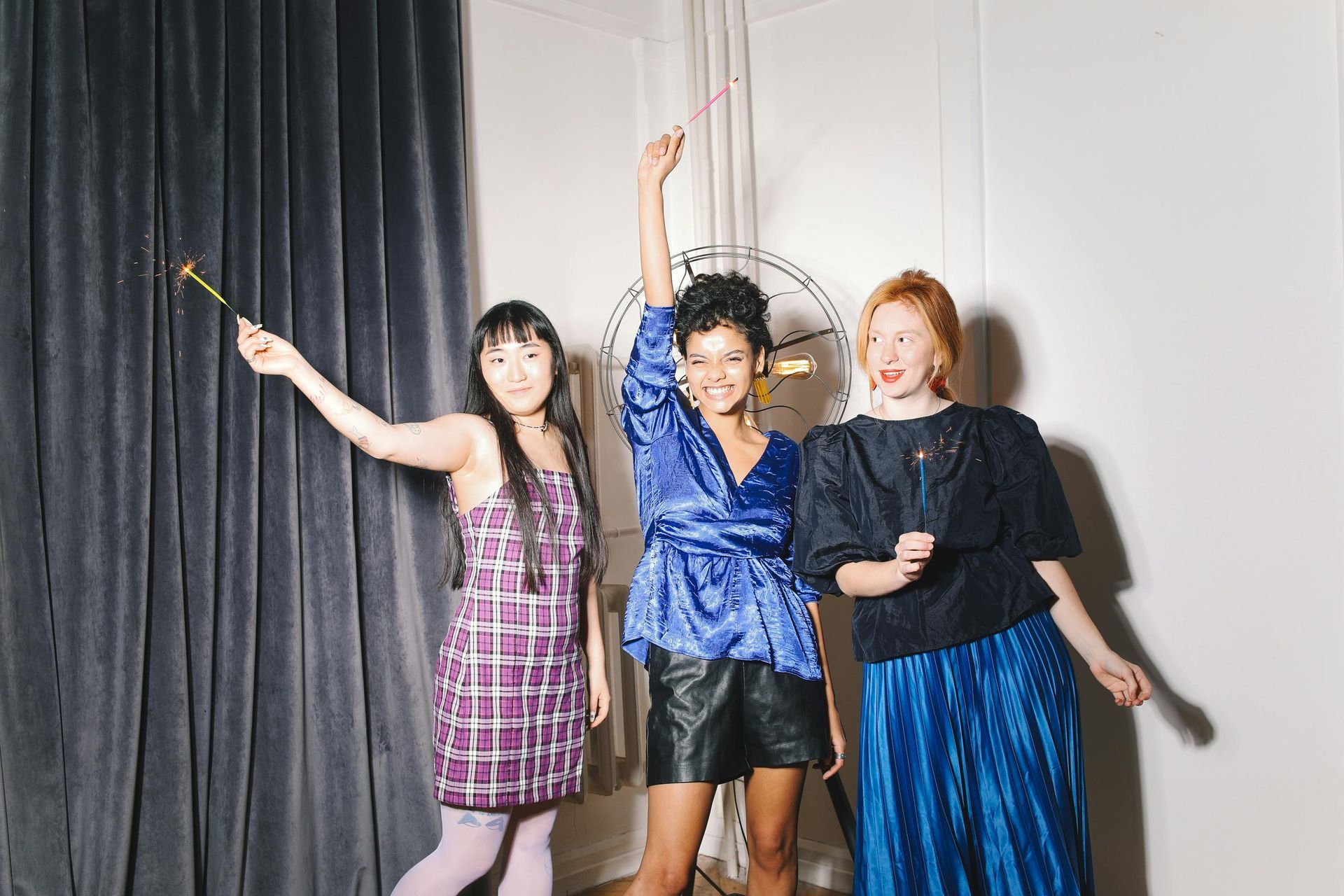 Three women are standing next to each other in a room holding sparklers.