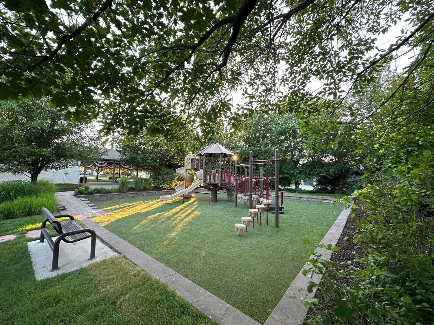 A playground in a park with a bench and trees in the background.