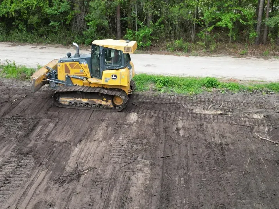 Yellow bulldozer grading a dirt lot beside a wooded road