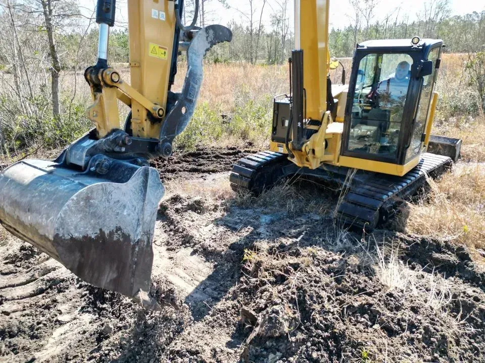 Two yellow excavators working in a muddy field, one with a large bucket in the foreground.