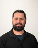 Smiling man with a dark beard in a black shirt against a light background