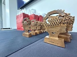 Three woven wooden trophies on a blue table, with red gift bags in the background.