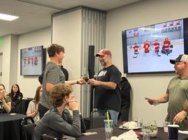 People in a meeting room exchange a handshake while watching a hockey game on wall-mounted screens.