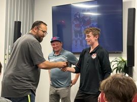 Man handing a small trophy to a smiling person in a classroom or meeting room