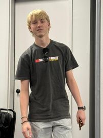 Person standing indoors in a dark T-shirt and light pants, facing the camera.