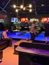 People playing pool in a dimly lit arcade with blue-lit tables and colorful game screens